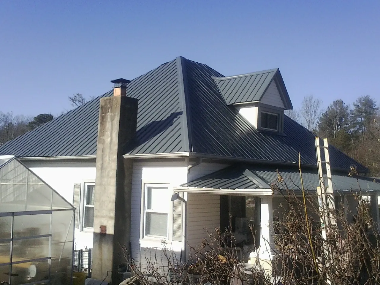 Dark blue standing seam metal roof on a white farmhouse with dormer — Slate & Tile Roof Repair by Roofing Brothers in Barnett