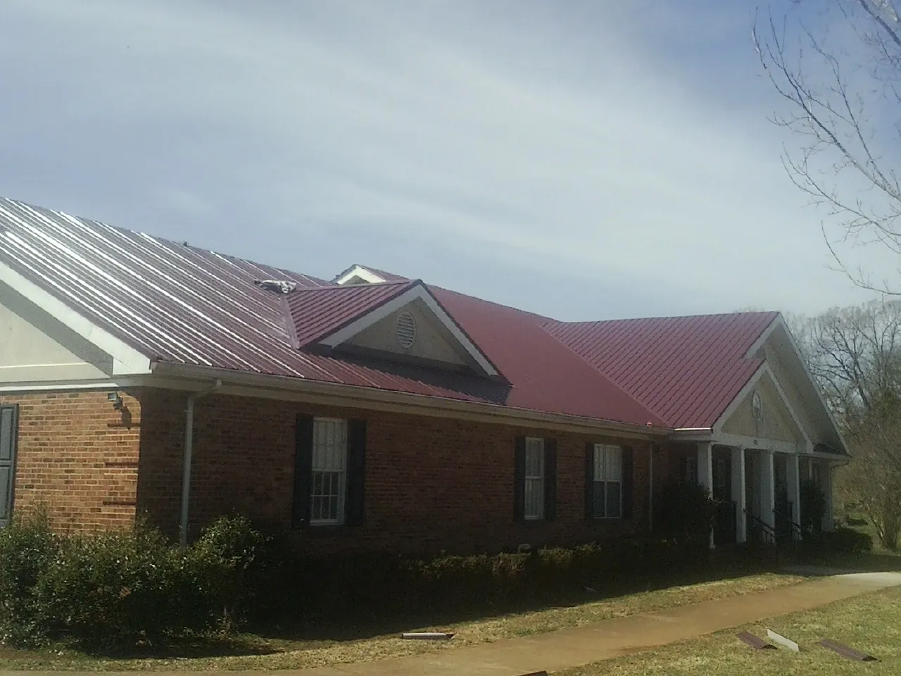 Red metal roof with gabled entries on a long brick building, from a Hail Damage Roof Repair job in Barnett
