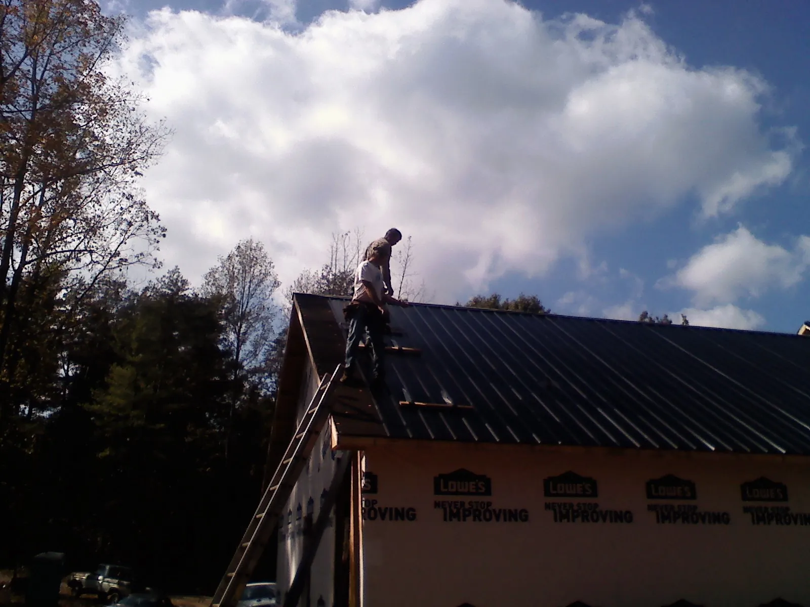 Roofer fastening dark metal panels high against a cloudy sky, from a Roof Inspection job in Barnett